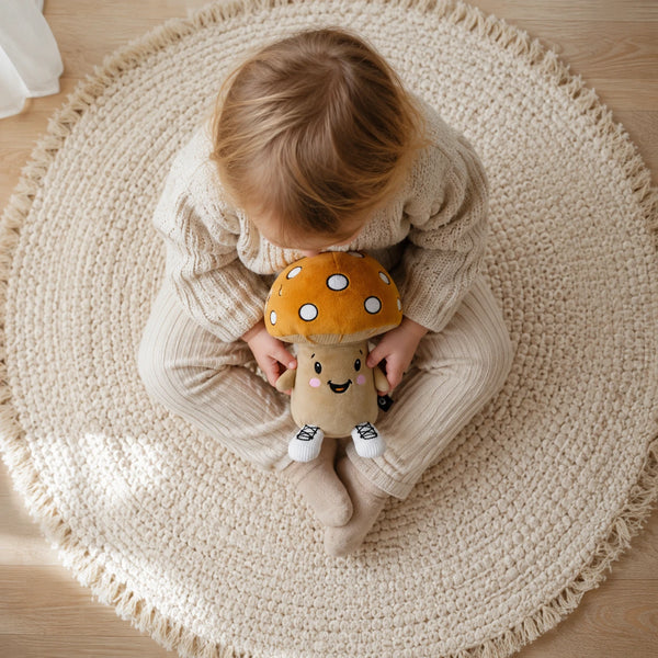 Kind sitzt auf einem Teppich und hält Lenabie Felix dem Pilz im Schoß. Das interaktive Audio-Kuscheltier für Kinder begleitet die Hörspiel- und Kuschelzeit mit Geschichten, Musik und altersgerechten Audioinhalten für das Kinderzimmer.