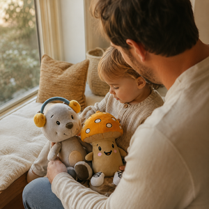 Vater und Kleinkind verbringen einen ruhigen Moment am Fenster mit den Lenabies Aaron dem Bären und Felix dem Pilz. Die interaktiven Kuscheltiere begleiten das gemeinsame Entdecken in einer warmen, gemütlichen Familienatmosphäre voller Geborgenheit und Nähe.
